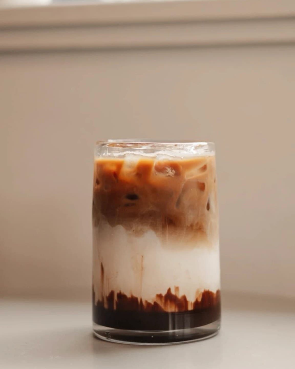 An iced latte in a clear glass, espresso and milk swirling in layers around the ice
